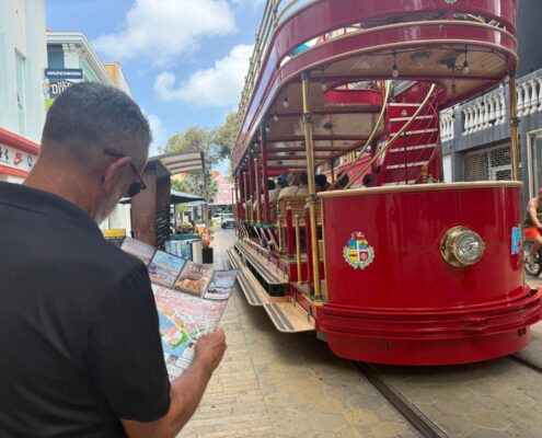 Visitor reading an Aruba Discovery guide map near the red Aruba streetcar in downtown Oranjestad