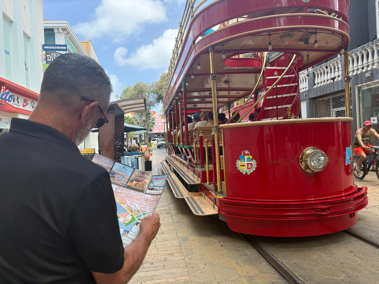 Visitor reading an Aruba Discovery guide map near the red Aruba streetcar in downtown Oranjestad